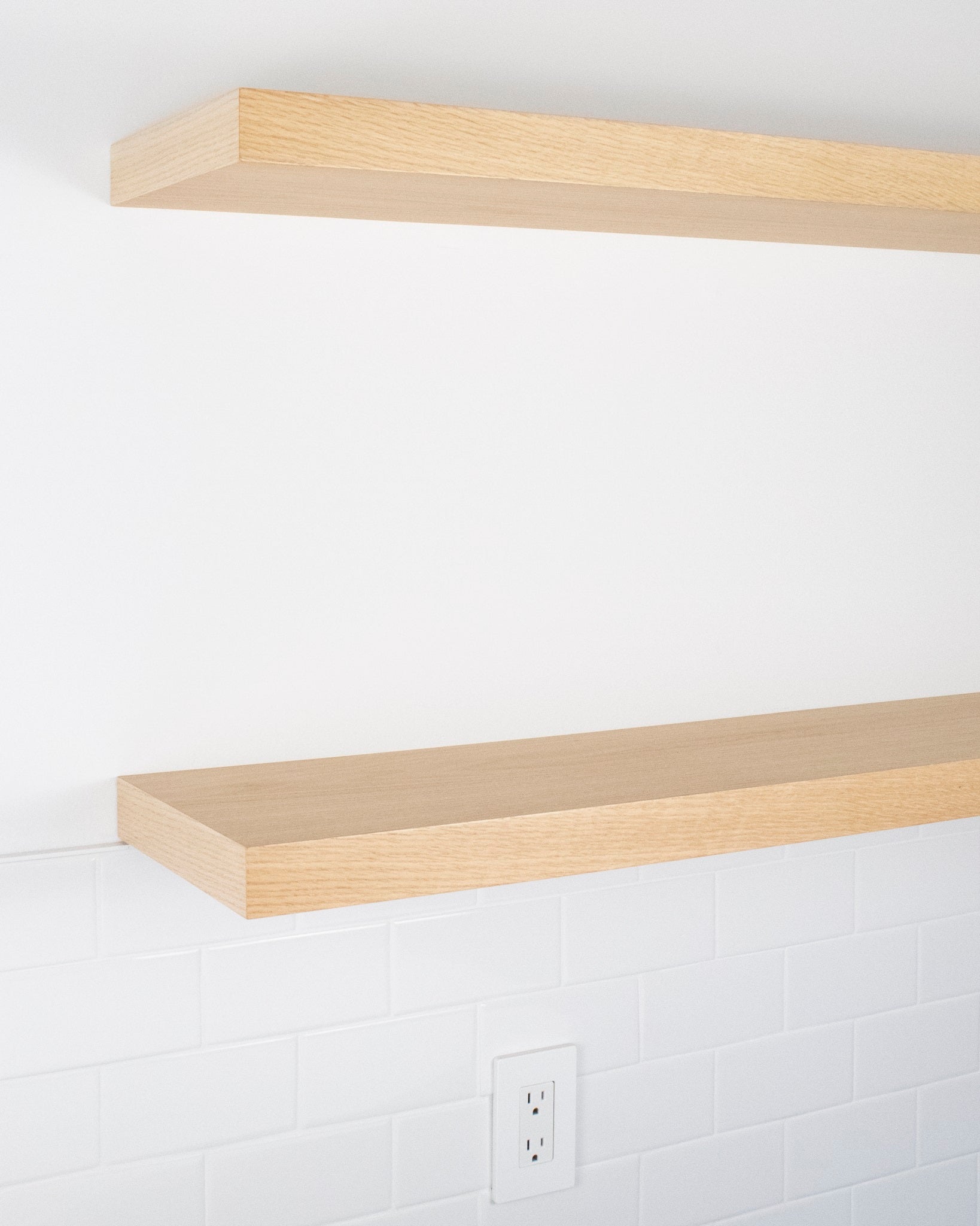 side angle view of two light oak floating shelves mounted one above the other on a wall