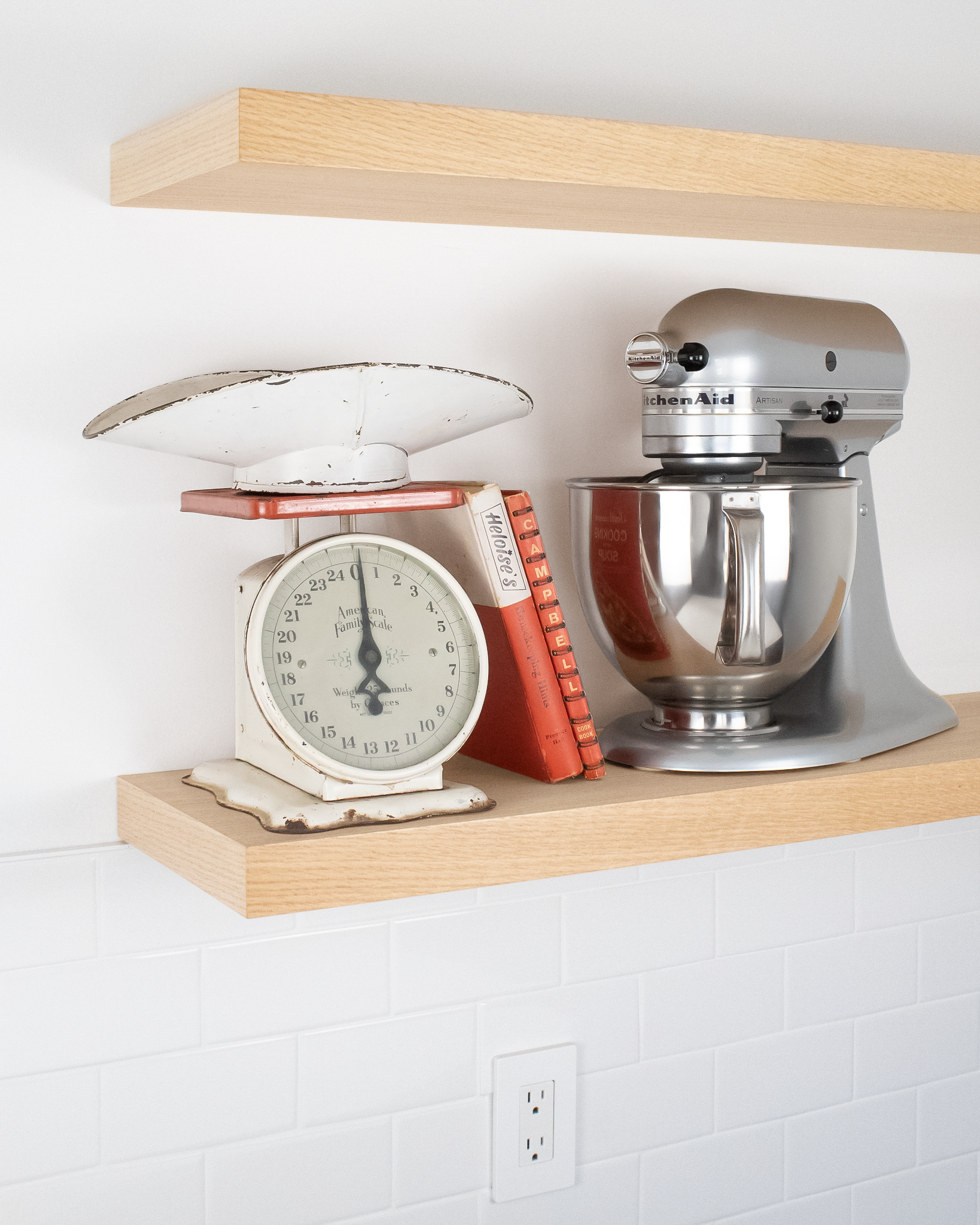 side angle view of two light oak floating shelves on a wall with the lower shelf holding a mixer and a scale