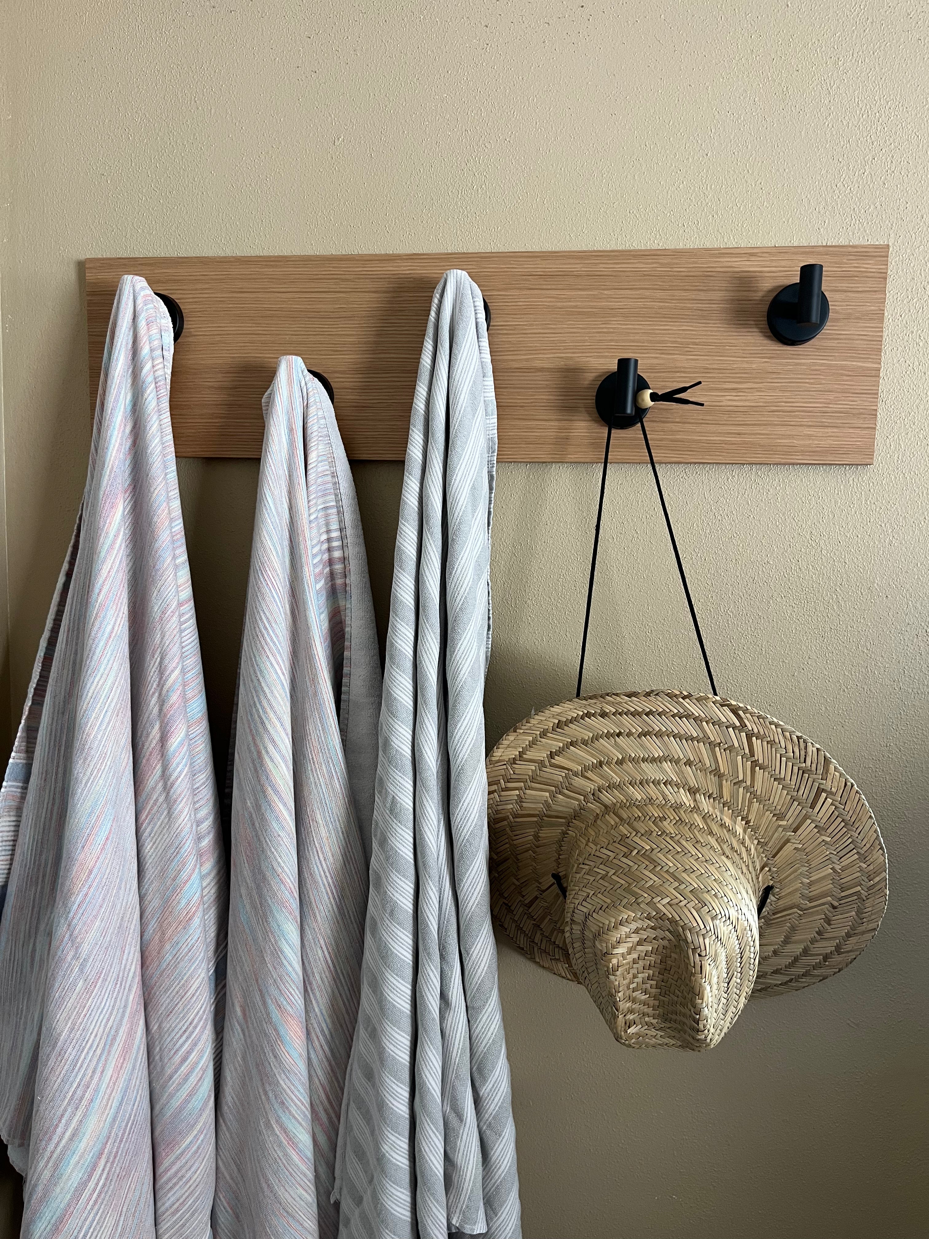 Wall rack in oak with 5 blacks hooks styled with striped towels and straw hat
