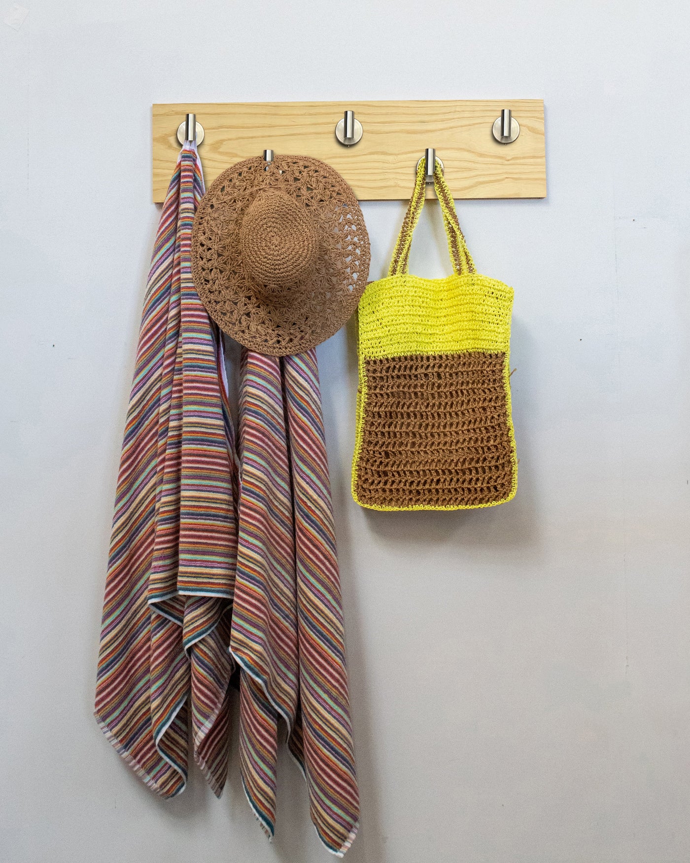 Ash wood wall hook rack with satin nickel hooks, striped towel, straw hat, and yellow bag on a white wall.