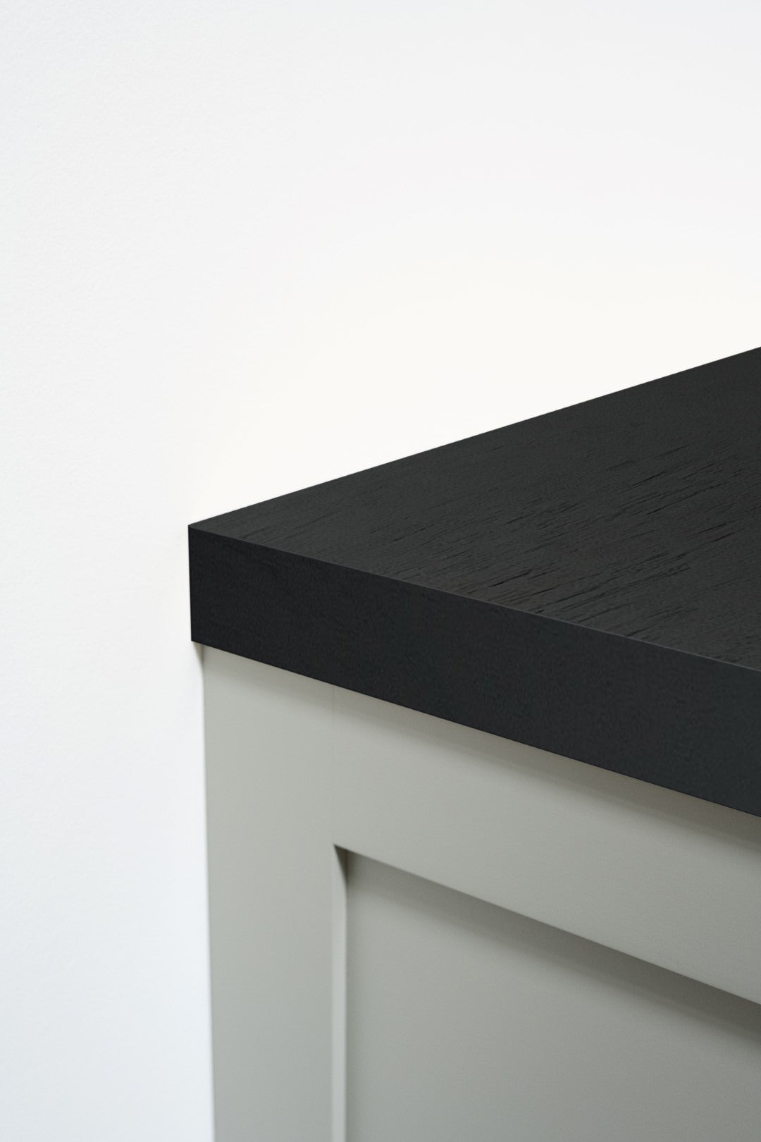 A close-up of a modern cabinet with a matte black countertop and light gray shaker-style doors against