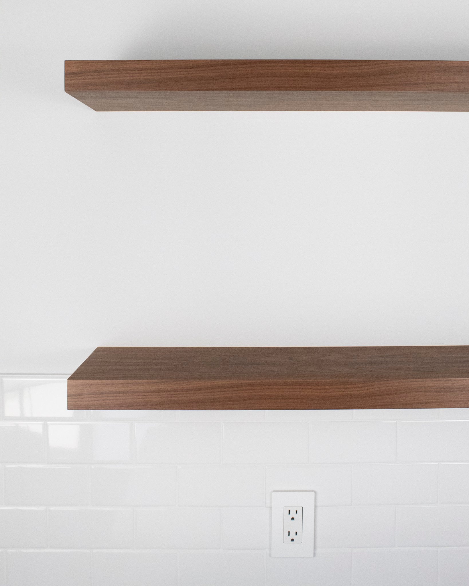 Front view of two walnut floating shelves mounted on a white wall.