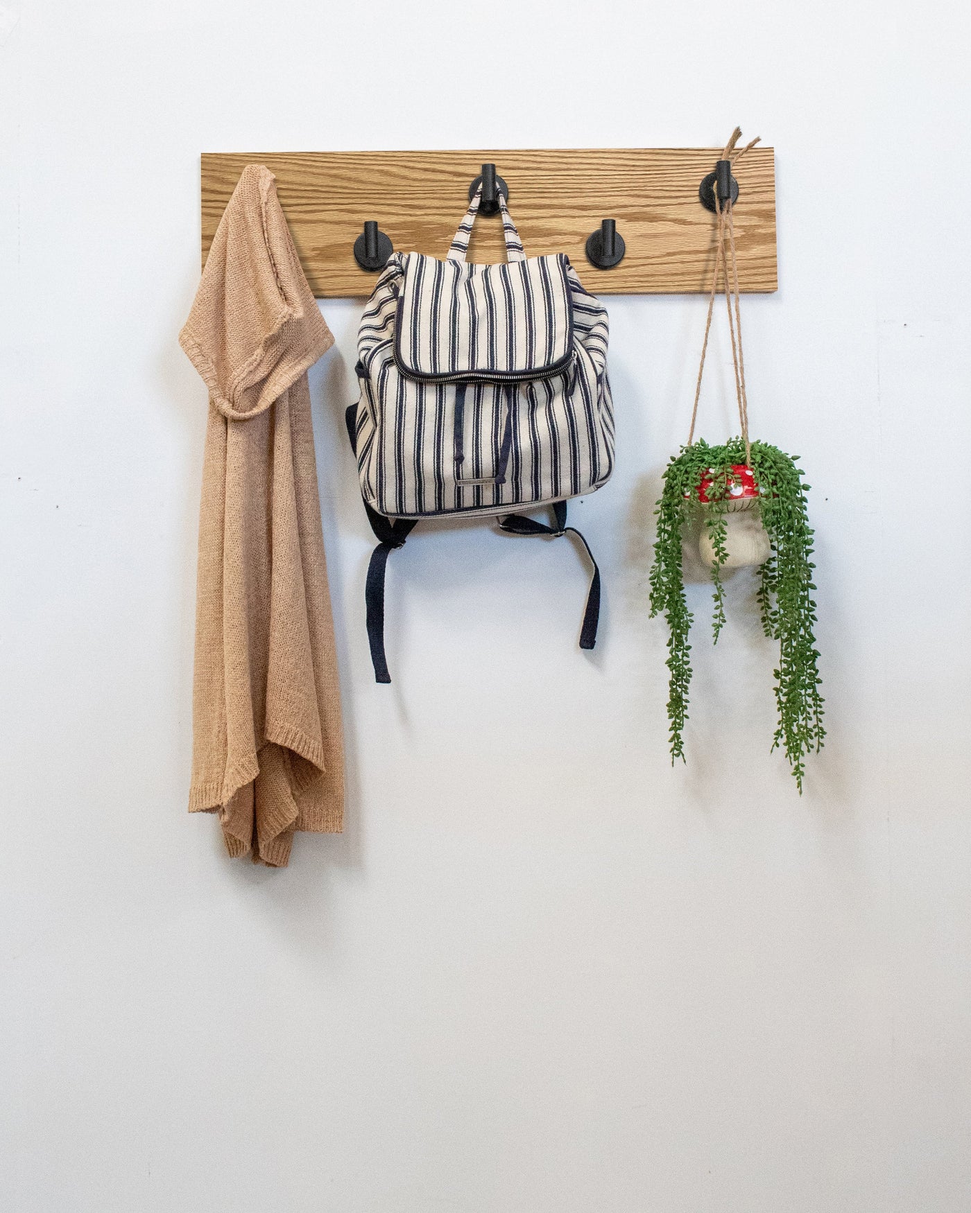 Red Oak wood wall hook rack matte black hooks with a backpack, coat, and plant