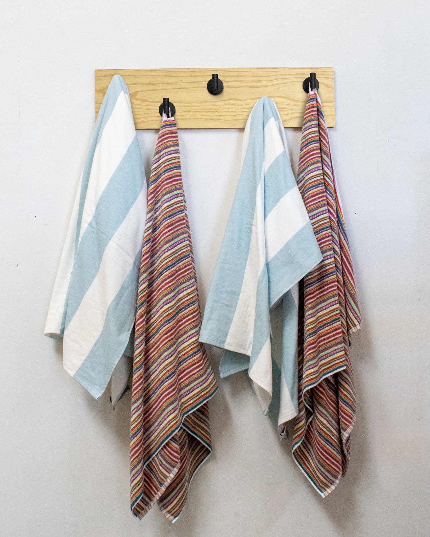 Striped towels hanging on Ash wood wall hook rack with matte black hooks.