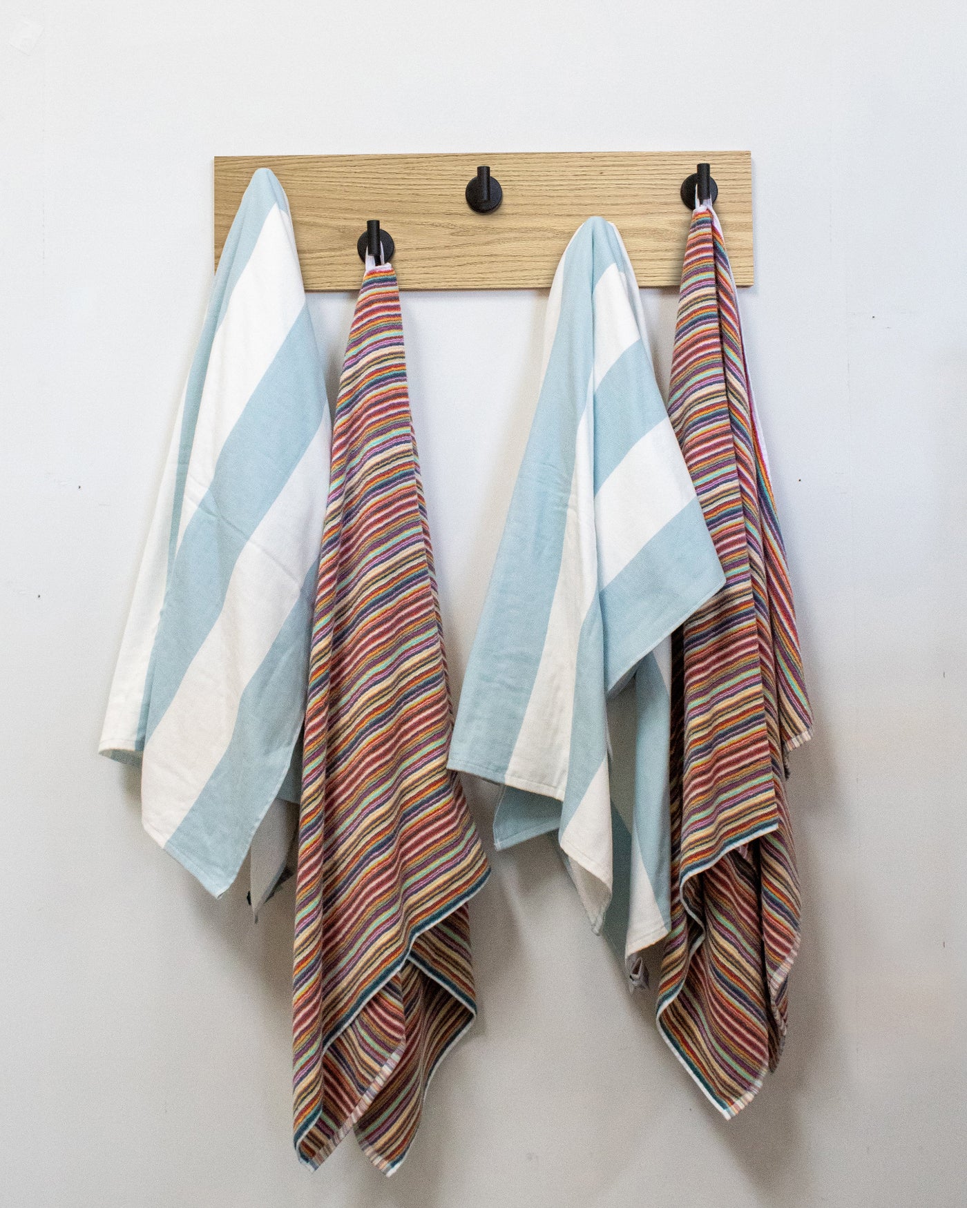 Striped towels hanging on a bleached oak wood wall hook rack with 5 matte black hooks
