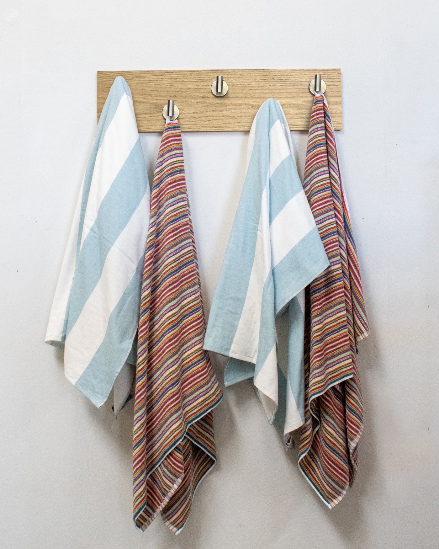 Striped towels hanging on a bleached oak wood wall hook rack with 5 satin nickel hooks