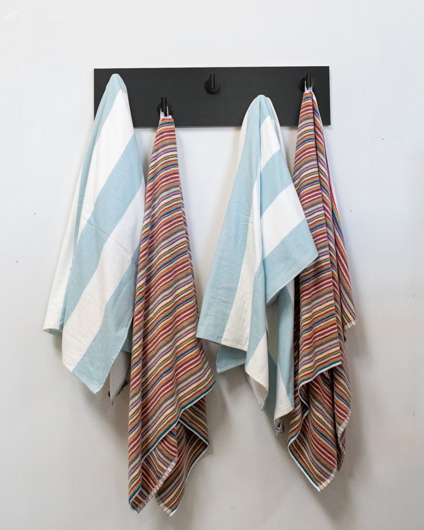 Striped towels hanging on a chocolate espresso oak wall hook rack with 5 matte black hooks