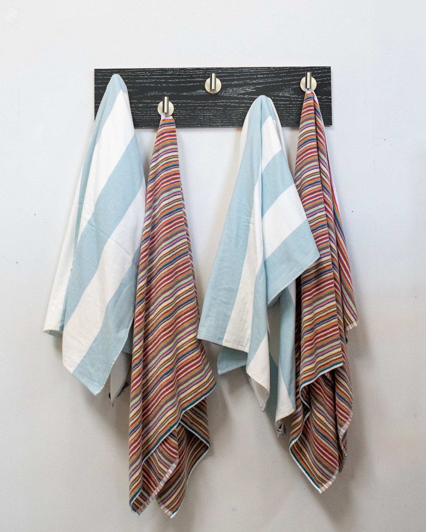 Striped towels hanging on a ebonized cerused oak wall hook rack with 5 satin nickel hooks