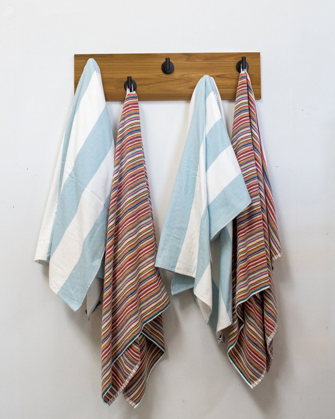 Striped towels hanging on a teak wood wall hook rack with 5 matte black hooks