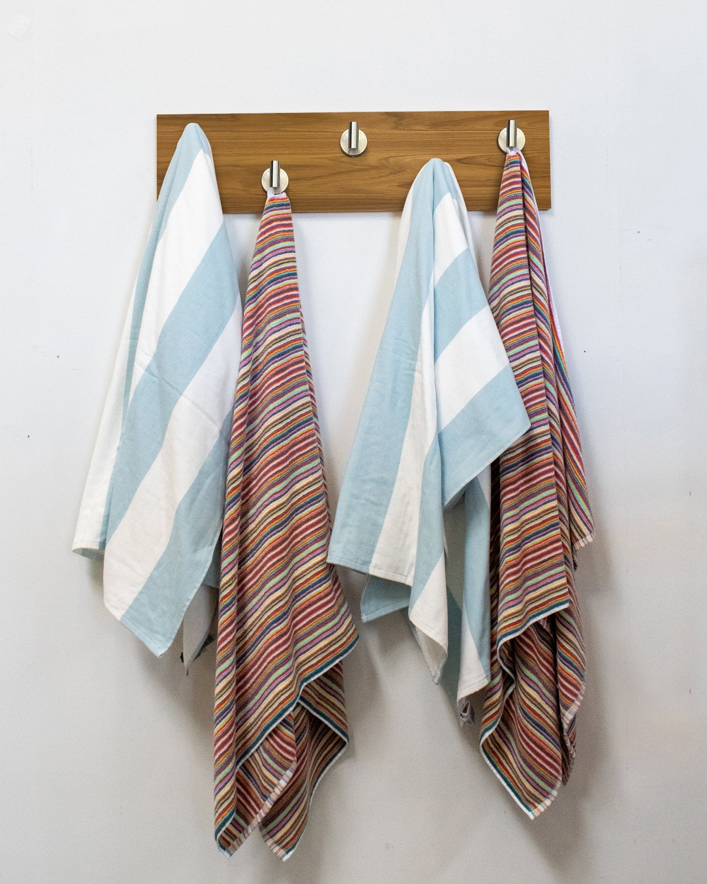 Striped towels hanging on a teak wood wall hook rack with 5 satin nickel hooks