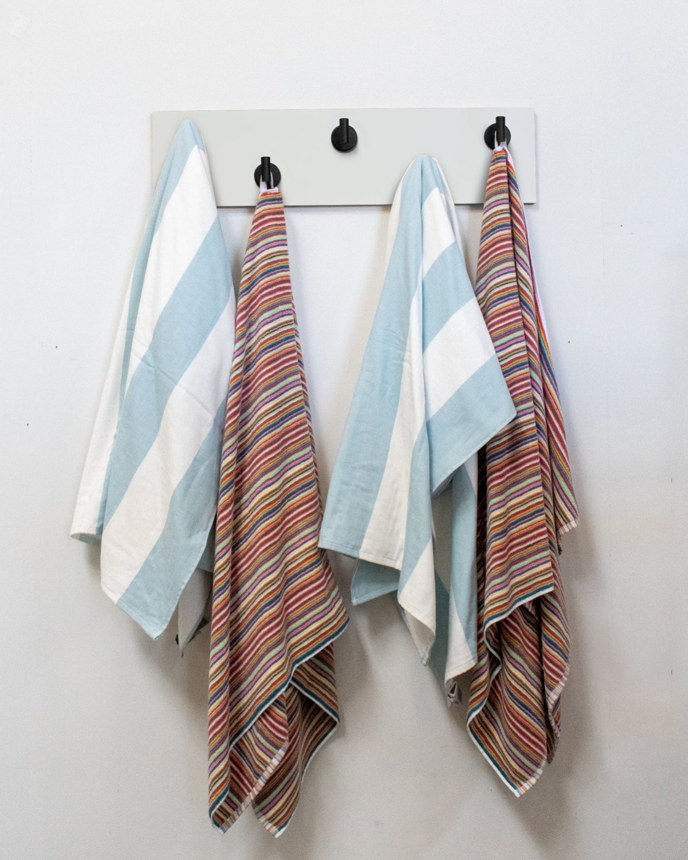 Striped towels hanging on a white wood wall hook rack with matte black hooks.