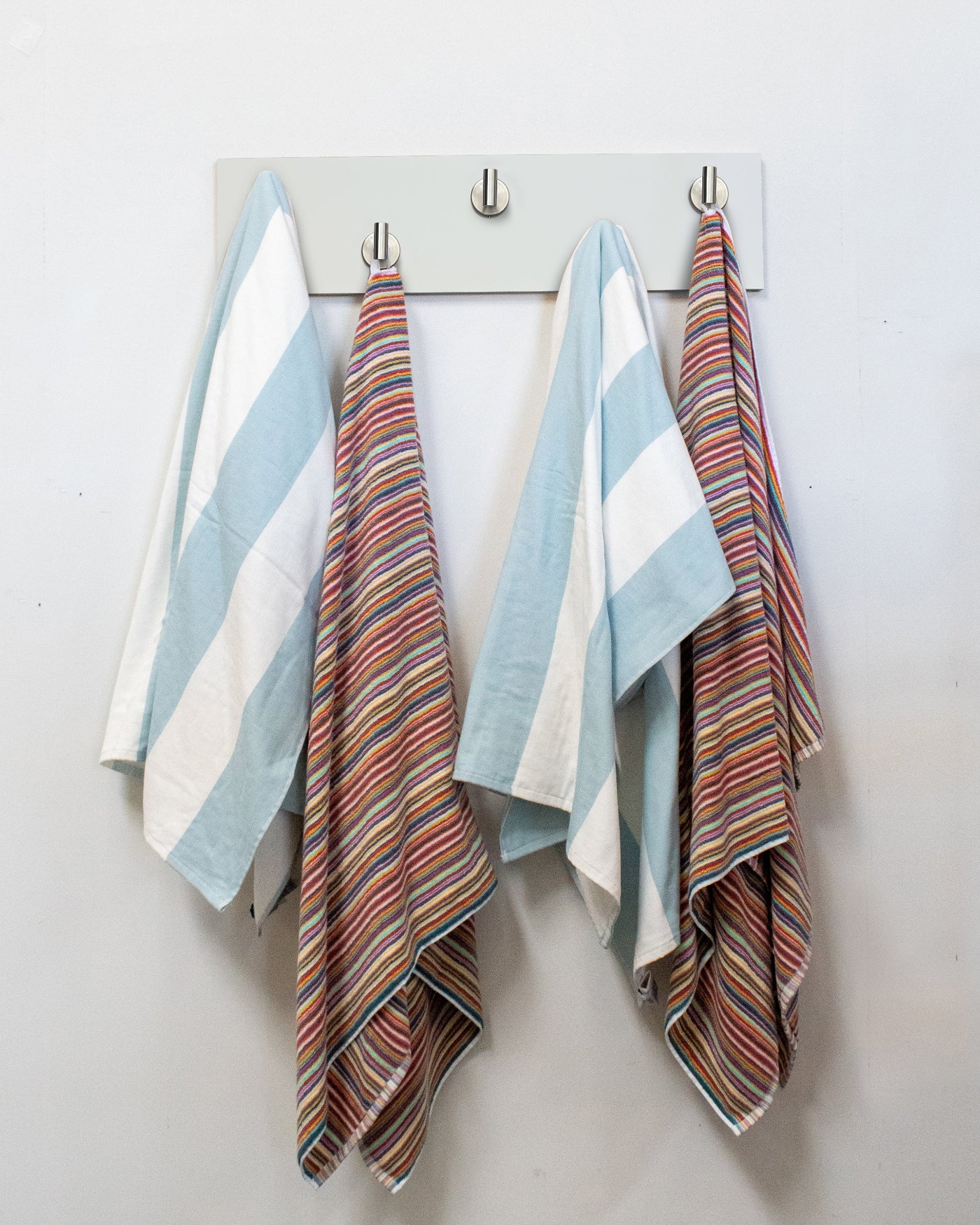 Striped towels hanging on a white wood wall hook rack with satin nickel hooks.