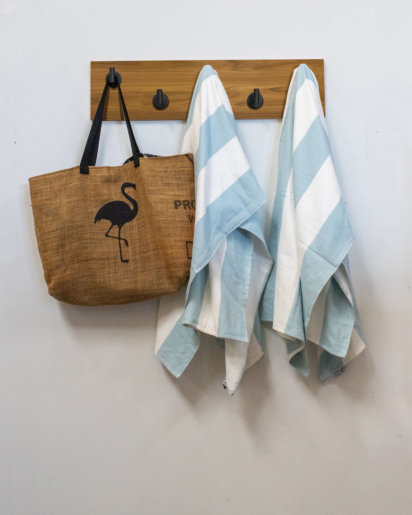 Teak wood wall hook rack brown tote bag with flamingo design and two striped towels hanging on 5 matte black hooks 