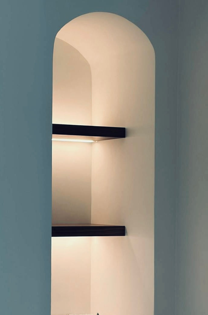 Walnut floating shelves with integrated lighting in an arched niche