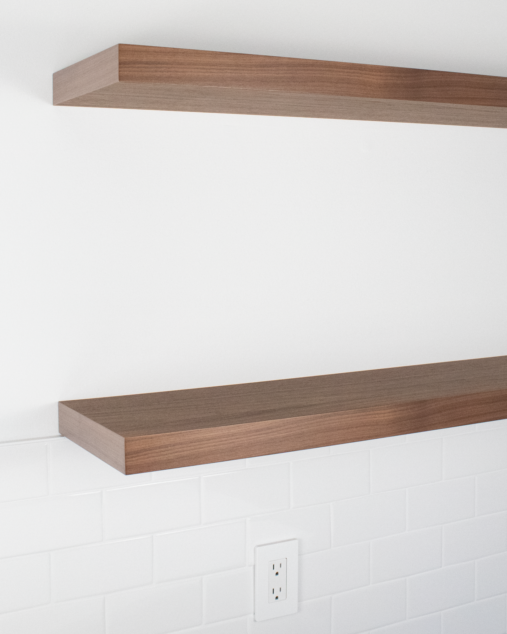 Angle view of two walnut wood floating shelves mounted on a white wall