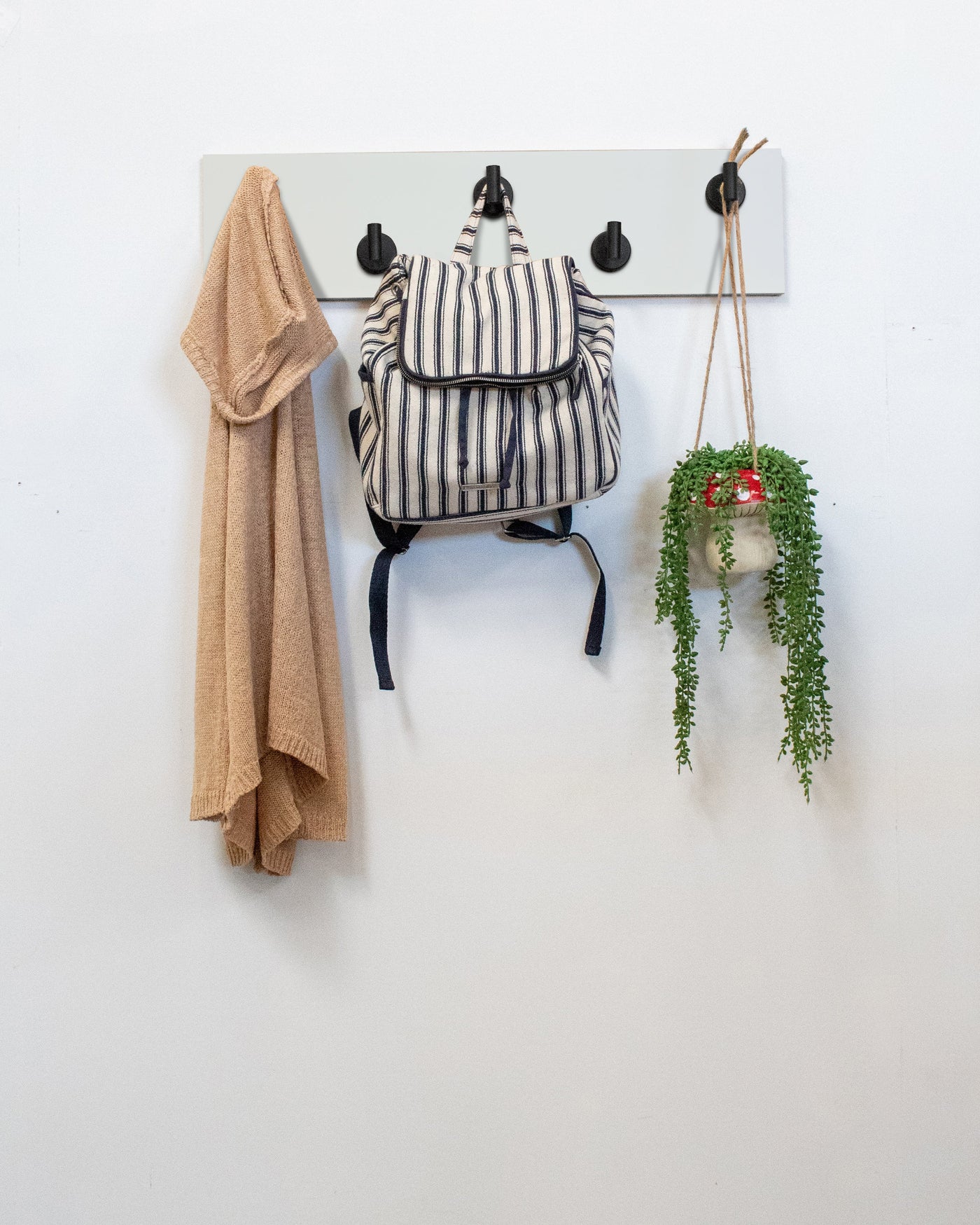 White Wood wall hook rack matte black hooks with a backpack, coat, and plant