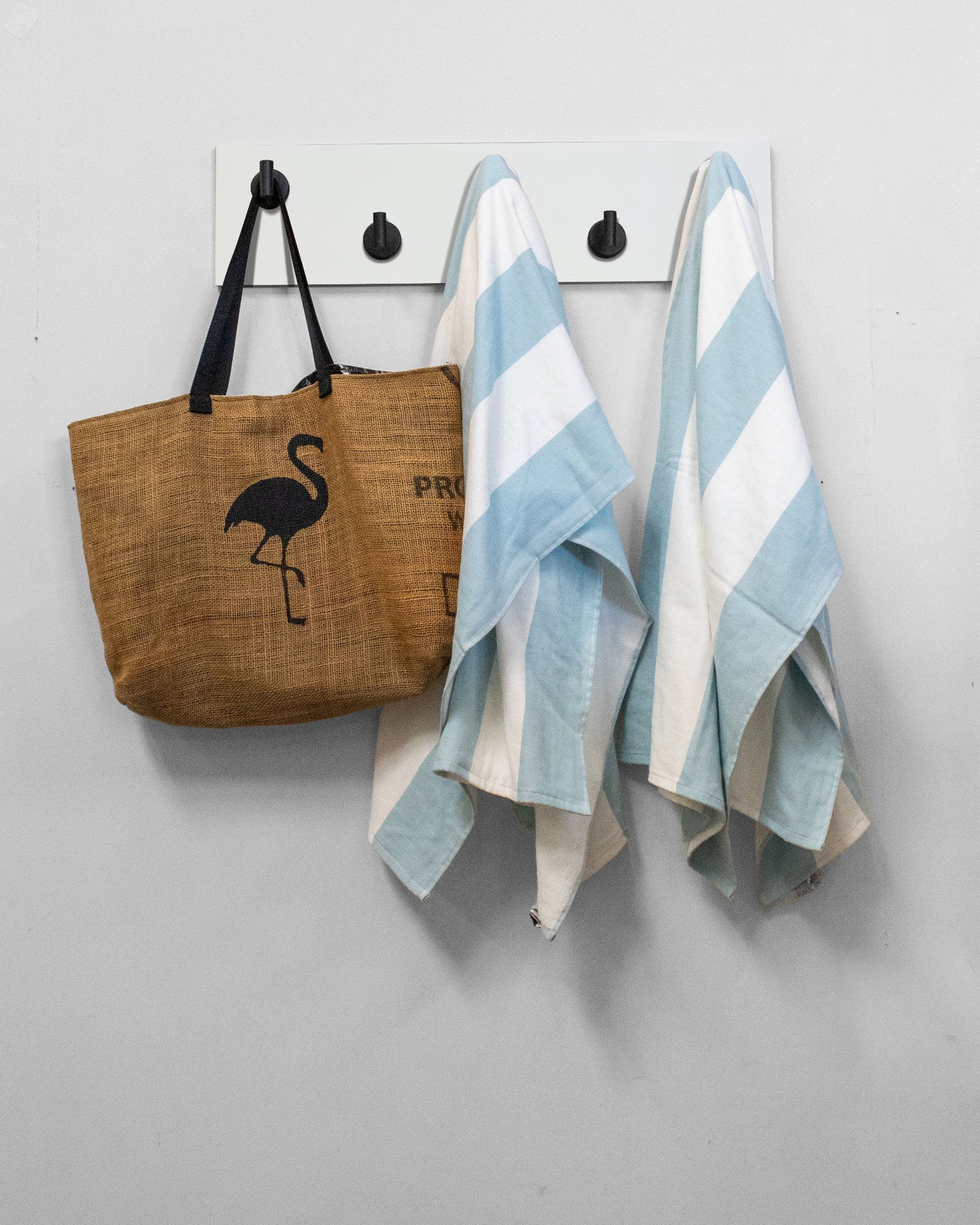 White wood wall hook rack brown tote bag with flamingo design and two striped towels hanging on 5 matte black hooks 