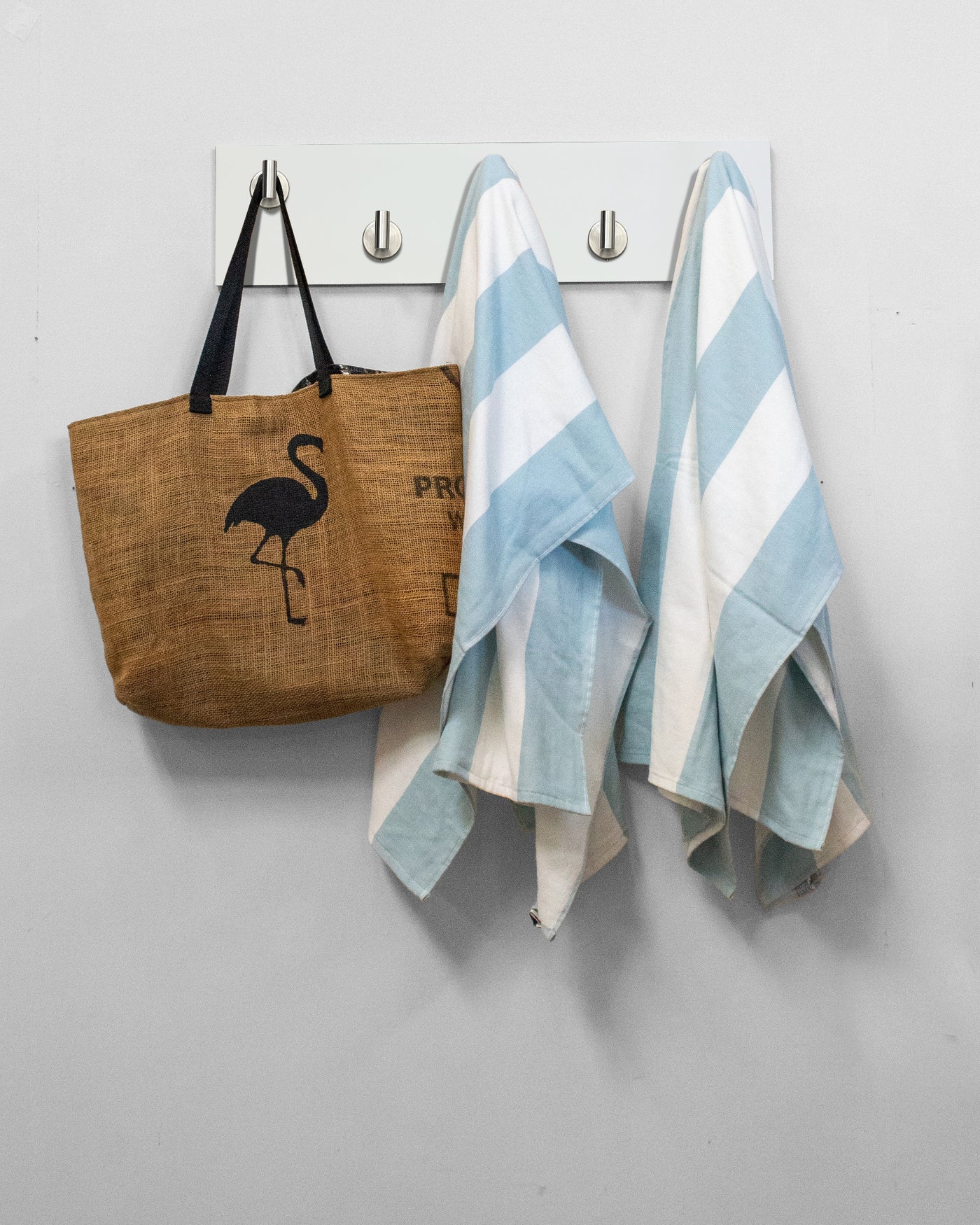 White wood wall hook rack brown tote bag with flamingo design and two striped towels hanging on 5 satin nickel hooks 