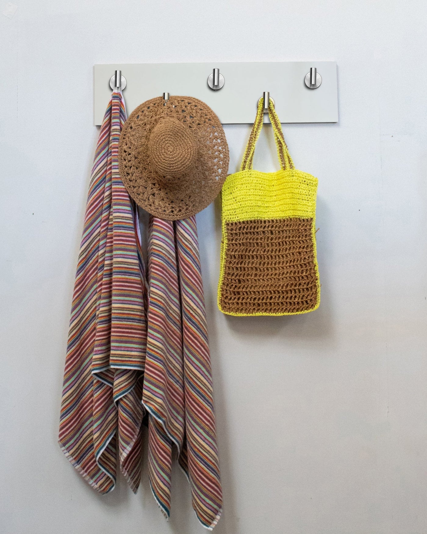 White wood wall hook rack with satin nickel hooks, striped towel, straw hat, and yellow bag on a white wall.