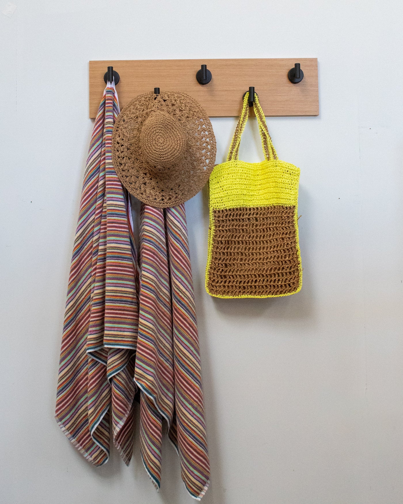 rift white oak wood wall hook rack with matte black hooks, striped towel, straw hat, and yellow bag